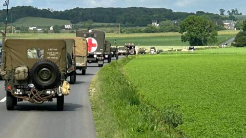 A long line of military green vehicles on a road in the green countryside of France