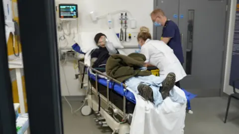 A patient lays in a hospital bed with nurses tending to him slightly out of focus