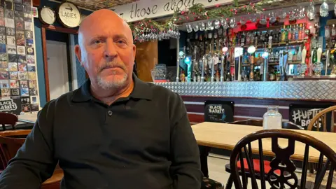 A bald man wearing a black top in a pub.