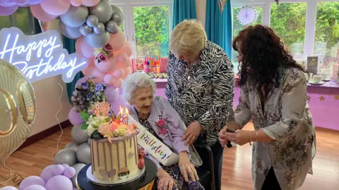 Shariqua Ahmed / BBC Olive Porritt with two women besides her birthday cake 