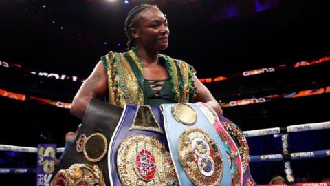 Claressa Shields smiles as she holds all her world title belts after a fight