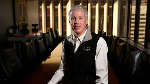 Getty Images Chris Wright wears a black vest over a white shirt, seated at a long conference table in a corporate office.