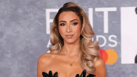 Getty Images GK Barry at the Brit Awards. She has long blonde hair which has been curled and wears a glam make up look and strapless black dress.