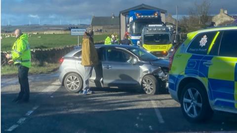 Emergency vehicles as the scene of a carcrash with a dented car quite visible 
