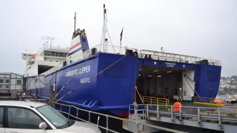 A blue ship with the words Commodore Clipper and Nassau written on the side, with its back ramp down. 