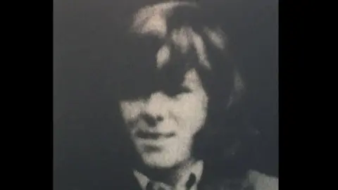 Black and white image of Francis Rice. He has long thick hair, wearing a shirt and jacket.