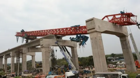 Reuters Collapsed crane seen lying across a concrete structure with train wreckage and emergency workers below