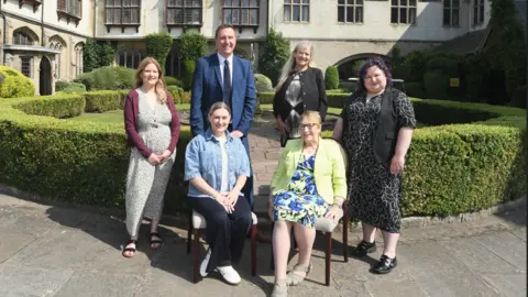 Gabrielle Boro, Richard Harrison, Hazel Brown (back) from the hotel and Michalina Kryska stand behind Faye Mackey and councillor Linda Bigham (both seated) at Coombe Abbey Hotel. They are stood in a garden area of the hotel.