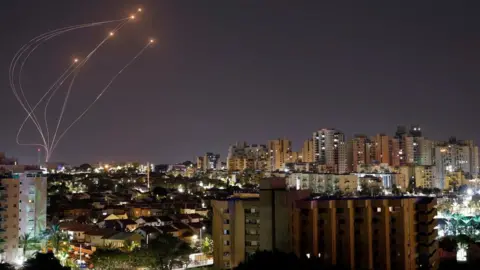 Reuters Streaks of light are seen as Israel's Iron Dome missile defence system intercepts rockets launched from the Gaza Strip, as seen from Ashkelon, southern Israel (7 April 2023)