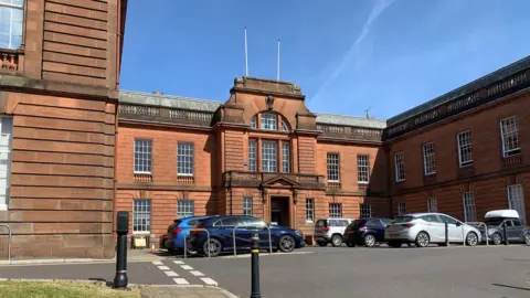 Council headquarters in Dumfries - a large sandstone building with lots of cars park outside