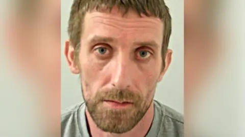 Lancashire Police Police custody shot of Antony Farren with a brown beard and hair wearing a grey t-shirt.