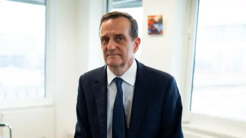 PA Media Stephen Parkinson in a suit tie in a brightly lit, white walled office