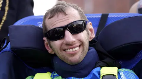 A close-up of Rob Burrow, smiling and wearing sunglasses 