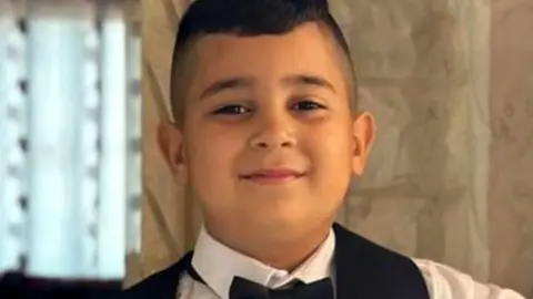 A family photo of eight-year-old Adam, who was shot by Israel's military, posing in a hallway wearing a bow tie and a waistcoat 
