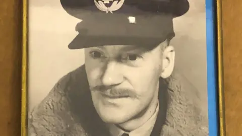 EMMAUS DOVER A World War 2 era photograph of Flying Officer Norman McEwan, in RAF uniform and flying jacket. He has a slim handlebar moustache.