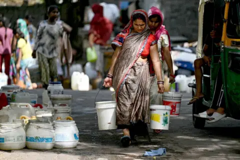 MONEY SHARMA/AFP Residents carry water containers after filling them from a municipal tanker in a low-income neighbourhood in Delhi on May 30, 2024