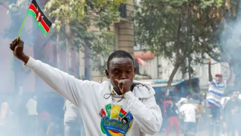 Reuters A man holds up a flag of Kenya as police use teargas to disperse protesters during a demonstration over police killings of people protesting against the imposition of tax hikes by the government in Nairobi, Kenya - 2 July 2024