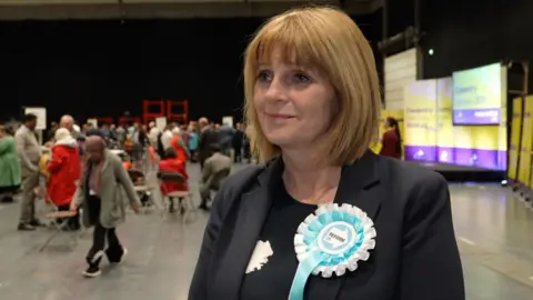 Jackie Gardiner wears a black jacket and dark dress. There is a Reform rosette pinned to her chest.