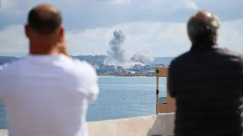 Adnan Abidi / Reuters Two people with their backs to the camera look out over the Tyre skyline as a plume of smoke rises over the city on Wednesday.