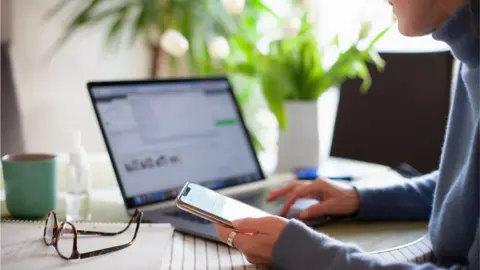 Getty Images A person sitting in front of a mobile phone and a laptop