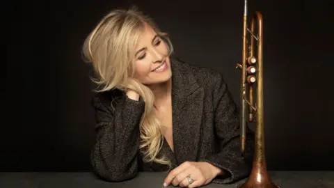 Bristol Beacon Alison Balsom sitting at a desk next to a trumpet as she looks at it.
