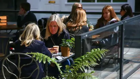 People sit at outdoor dining tables set up outside a restaurant at Covent Garden in London, UK