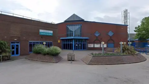 Google An image of Goole Leisure Centre taken from Google StreetView. It is a red brick building with bright blue windows and doors. There are raised beds with shrubs in, built in the same bricks