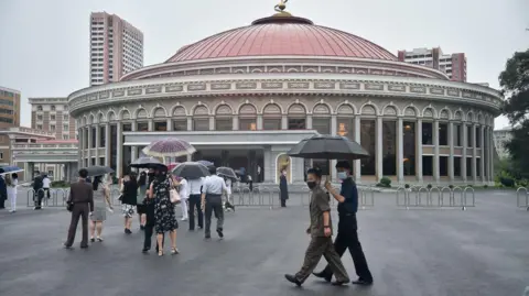 Getty-mensen met parasols lopen voor een groot rond gebouw met een koepelvormig dak.