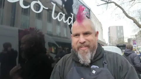 Man with pink mohawk smiles at the camera. 