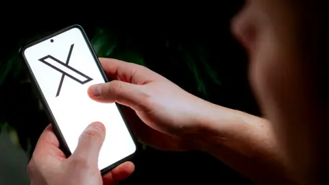 Getty Images A person holding a phone with the X logo on the screen