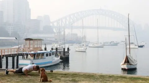 Getty Images A man does push-ups next to a dog in front of the Sydney Harbour Bridge, which is obscured by thick smoke