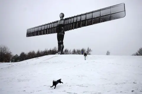 Reuters A black dog running in the snow at the foot of the Angel of the North sculpture. The Angel is dusted in snow.