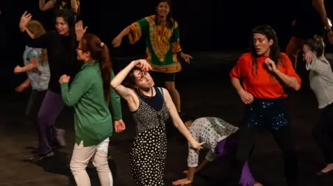 Jumped Up Theatre Women dancing in a studio, wearing colourful clothing.