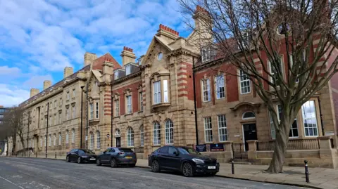 A large building on a city street with cars parkd outside. 