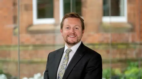 British Council Dr Ian Collen, with beard, in white shirt, paisley tie and black jacket