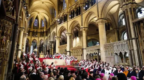 PA Media A wide view inside the cathedral showing groups of robed clergy seated on raised platforms and many people gathered in pews below as the Archbishop of Canterbury Dame Sarah Mullally speaks during the enthronement.