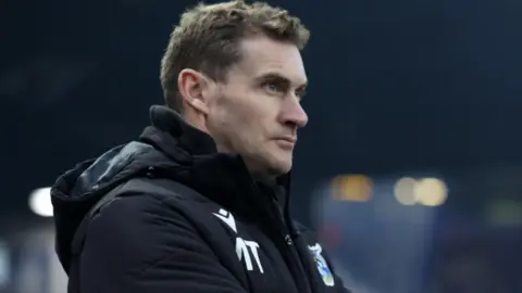 Getty Images A close-up of Matt Taylor in a thick black winter coat against a blurred background, looking thoughtfully into the distance to the left of camera