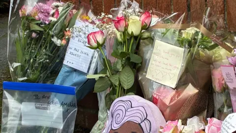 A close up shot of some of the floral tributes, some of which have notes attached. 
