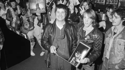 Mirrorpix via Getty Images Ozzy Osbourne in a record shop surrounded by fans.