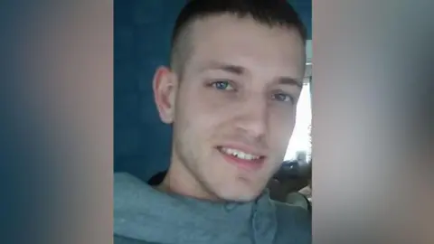 Undated close up image of Shane Graham who has blue eyes, short brown hair and stubble. He is smiling. 