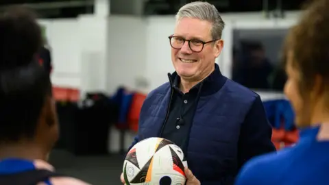 Getty Images Labour leader Sir Keir Starmer holds a football while talking with members of the women's under-17 England team