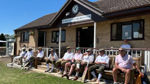 People sat on benches outside Oundle Town Cricket Club's clubhouse