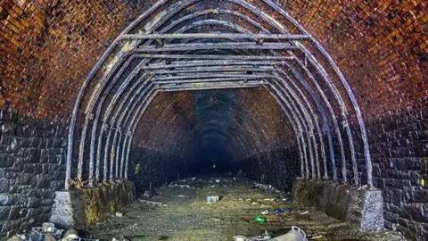 @Forgottenrelics a red brick railway tunnel covered with some gray metal hose.  