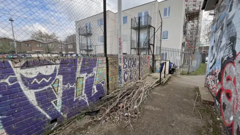 A low brick wall with graffiti all over it and a building behind it. 