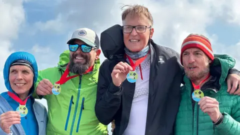 Four people at the finish line, smiling with their medals.
