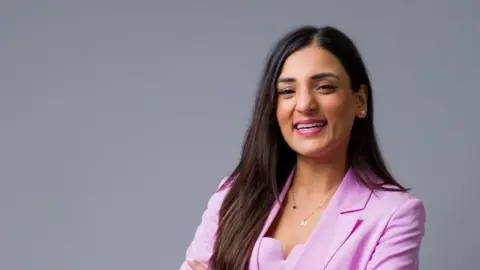 Anastasia Jobson con cabello negro largo y con una chaqueta rosa, el Dr. Suglani sonríe mientras mira a la cámara.