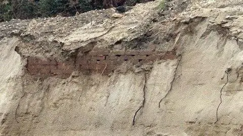 National Trust Sandy beach cliffs with brick work seen in a line along the sand