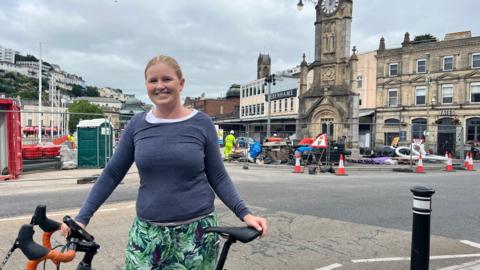 Beth Huntley with her bicycle in front of the regeneration works in Torquay