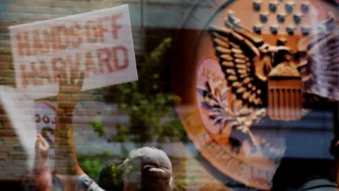 Reuters A man holds a sign outside the courthouse. You can see him in the reflection of the glass. His sign reads 'hands off Harvard'. The seal of the US government is in the foreground