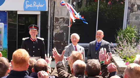 PA Media King Charles throws a bright coloured ball with ribbons into a crowd of men waiting to grab it